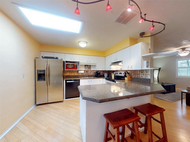 kitchen with backsplash, white cabinets, light hardwood / wood-style floors, kitchen peninsula, and stainless steel appliances