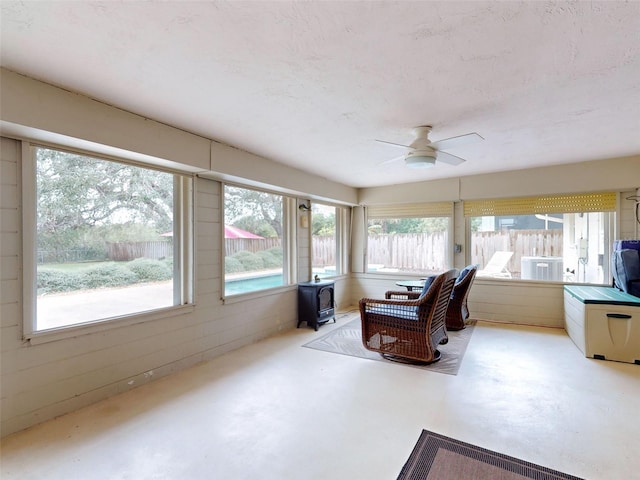 sunroom with a wood stove, ceiling fan, and plenty of natural light