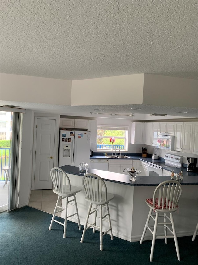 kitchen with white cabinetry, a kitchen breakfast bar, white appliances, and kitchen peninsula