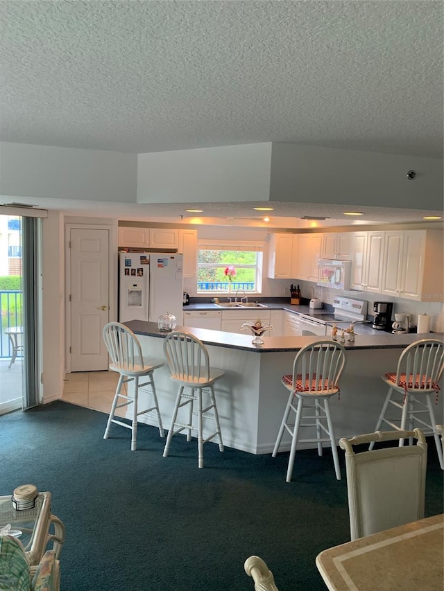 kitchen with a kitchen breakfast bar, white appliances, white cabinets, and kitchen peninsula