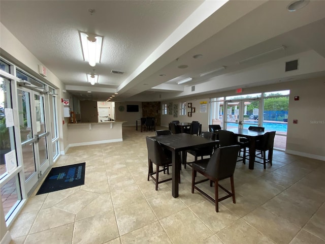 dining room featuring a textured ceiling, light tile patterned floors, a raised ceiling, and french doors