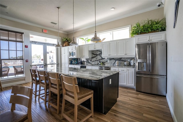 kitchen featuring a center island, white cabinets, appliances with stainless steel finishes, decorative light fixtures, and light stone counters