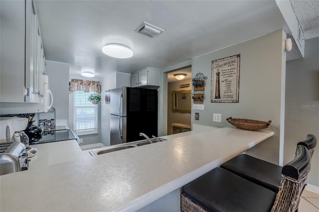 kitchen with stainless steel refrigerator, kitchen peninsula, white cabinetry, and sink