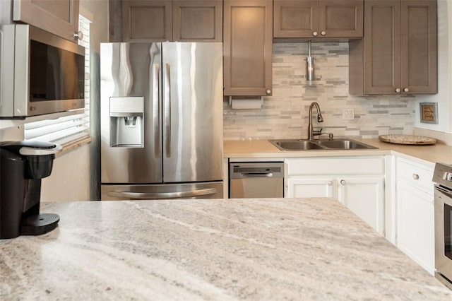 kitchen with backsplash, white cabinets, sink, light stone counters, and stainless steel appliances