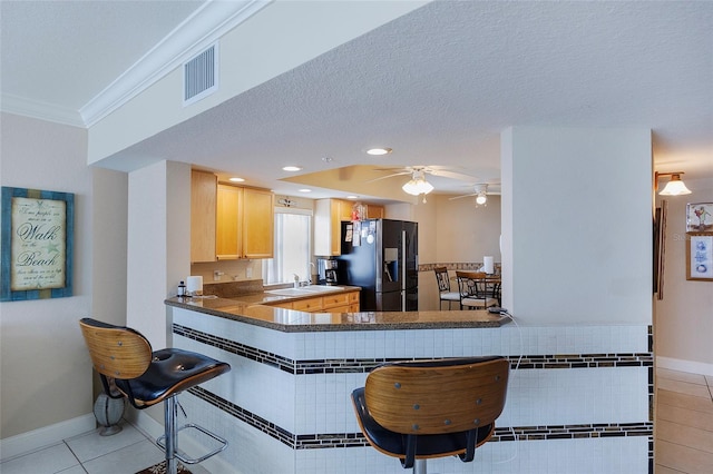 kitchen featuring light tile patterned flooring, a textured ceiling, kitchen peninsula, and stainless steel fridge