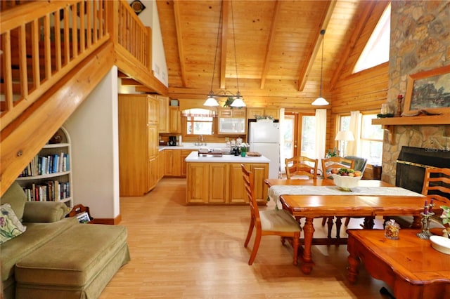 dining room featuring light wood-type flooring, beam ceiling, built in features, wooden ceiling, and a stone fireplace