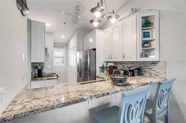 kitchen with pendant lighting, vaulted ceiling, stainless steel fridge with ice dispenser, decorative backsplash, and white cabinetry