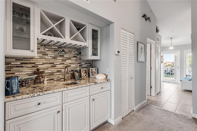 bar featuring light stone countertops, backsplash, light colored carpet, decorative light fixtures, and white cabinets