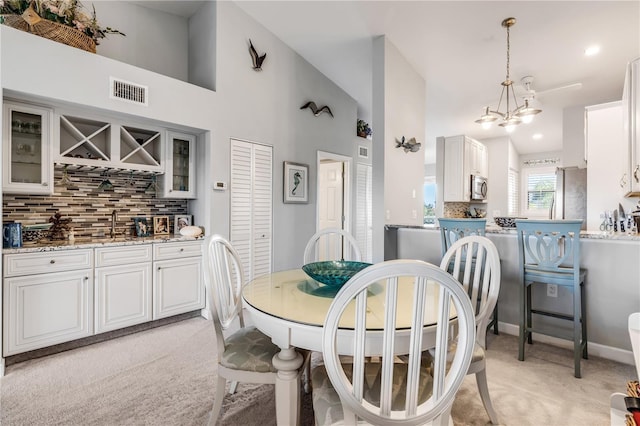 carpeted dining room featuring sink, high vaulted ceiling, and an inviting chandelier