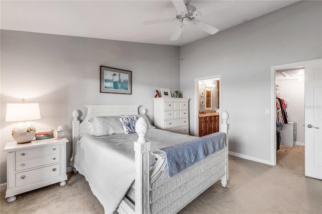 bedroom with light carpet, a walk in closet, ceiling fan, connected bathroom, and a closet