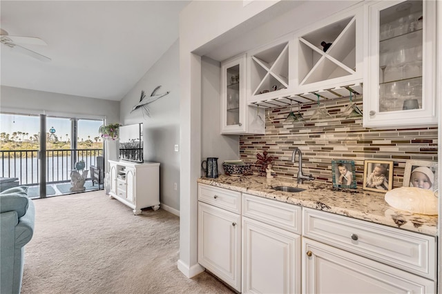 kitchen featuring light carpet, tasteful backsplash, sink, a water view, and white cabinetry