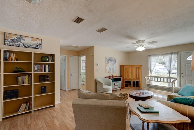 living room with ceiling fan, a textured ceiling, and light wood-type flooring