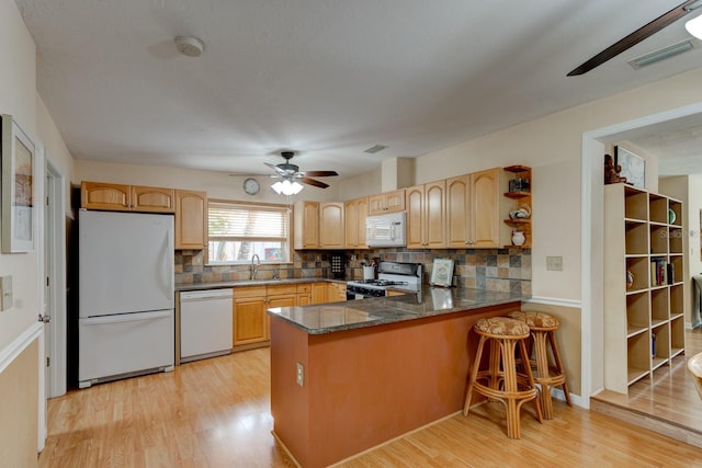 kitchen featuring a kitchen breakfast bar, backsplash, kitchen peninsula, light hardwood / wood-style floors, and white appliances