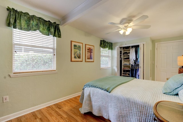 bedroom featuring beam ceiling, a closet, light hardwood / wood-style flooring, and ceiling fan