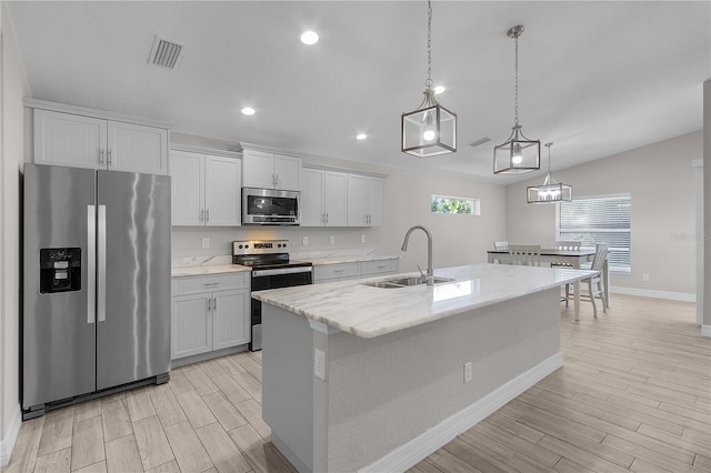 kitchen with a kitchen island with sink, hanging light fixtures, sink, white cabinetry, and stainless steel appliances