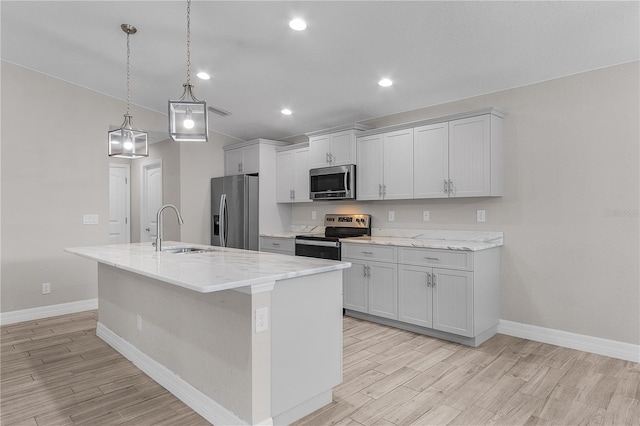 kitchen with light stone countertops, sink, pendant lighting, a center island with sink, and appliances with stainless steel finishes