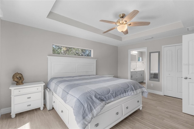 bedroom with a raised ceiling, connected bathroom, ceiling fan, and light hardwood / wood-style floors