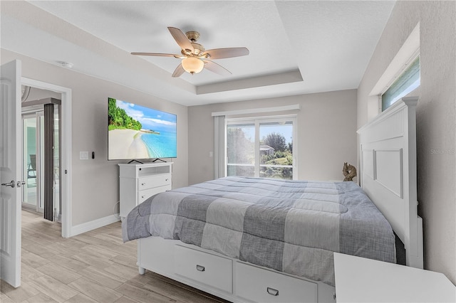 bedroom with a raised ceiling, multiple windows, ceiling fan, and light hardwood / wood-style floors