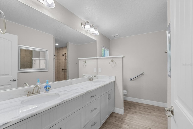 bathroom featuring hardwood / wood-style floors, vanity, toilet, tiled shower, and a textured ceiling