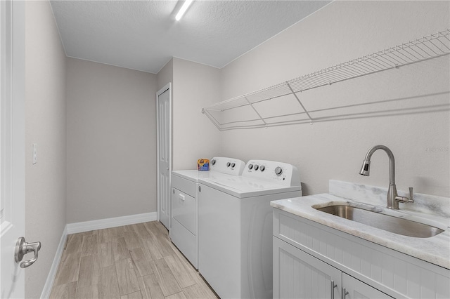 laundry area with cabinets, sink, light hardwood / wood-style flooring, washer and dryer, and a textured ceiling