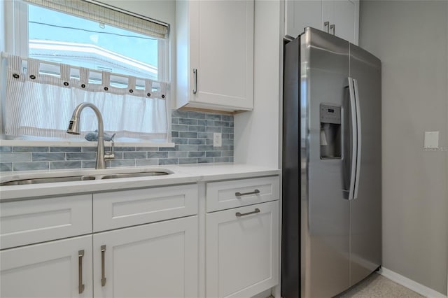 kitchen with backsplash, stainless steel fridge, white cabinets, and a sink