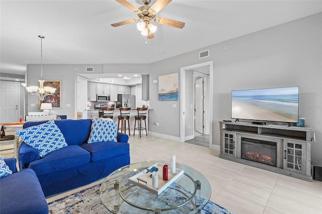 tiled living room with ceiling fan with notable chandelier