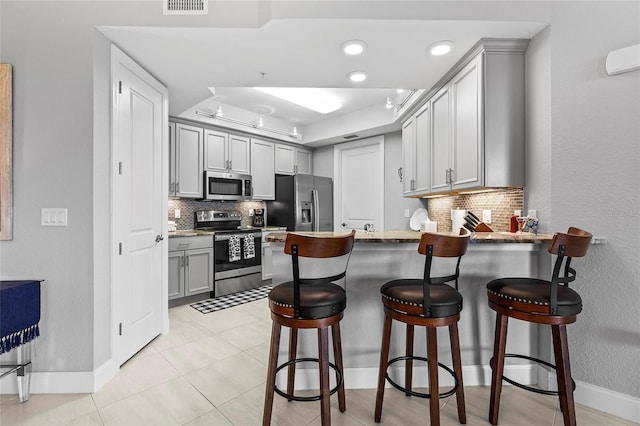 kitchen with kitchen peninsula, appliances with stainless steel finishes, a breakfast bar, and tasteful backsplash