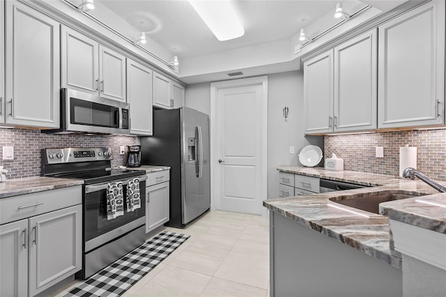 kitchen with stainless steel appliances, light stone counters, tasteful backsplash, and sink