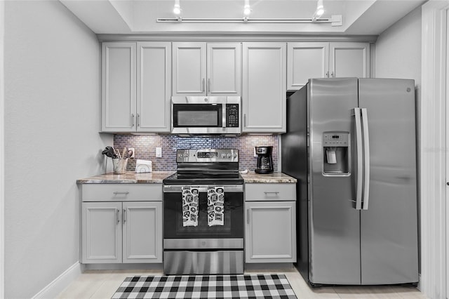 kitchen with backsplash, stainless steel appliances, light stone counters, and gray cabinetry