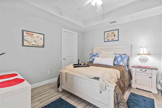 bedroom featuring a raised ceiling, ceiling fan, and light hardwood / wood-style flooring