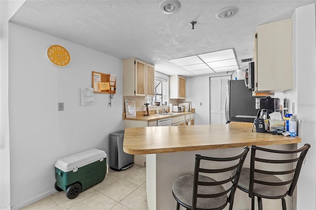 kitchen with appliances with stainless steel finishes, a kitchen bar, light brown cabinets, kitchen peninsula, and light tile patterned floors