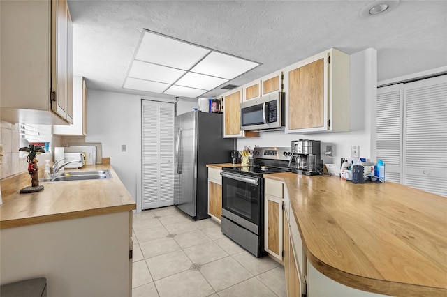 kitchen with sink, light brown cabinetry, light tile patterned floors, and appliances with stainless steel finishes