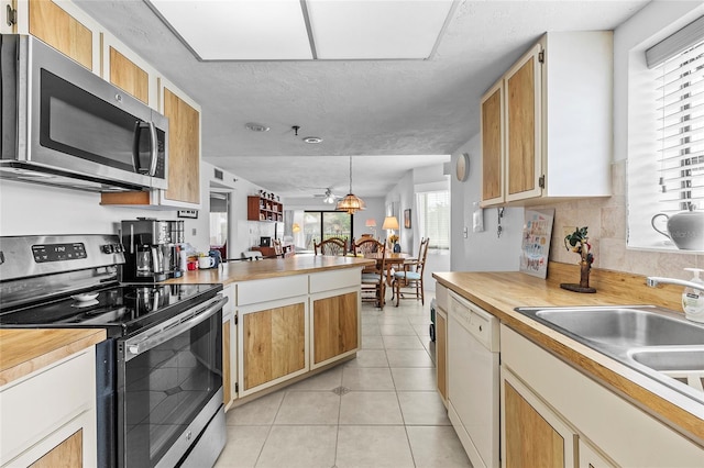 kitchen with appliances with stainless steel finishes, sink, decorative light fixtures, light tile patterned floors, and a textured ceiling