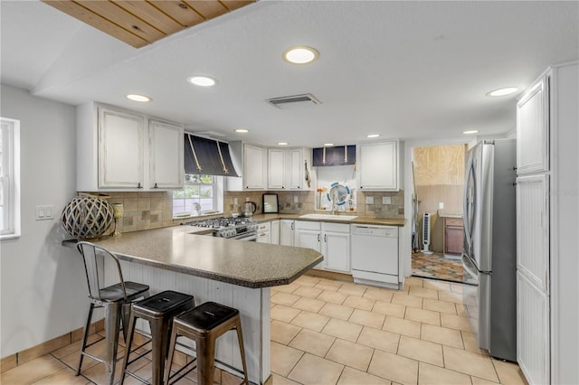 kitchen with white cabinetry, wall chimney exhaust hood, kitchen peninsula, a kitchen bar, and appliances with stainless steel finishes