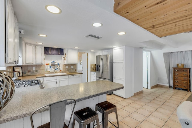 kitchen featuring kitchen peninsula, a kitchen breakfast bar, backsplash, sink, and white cabinetry