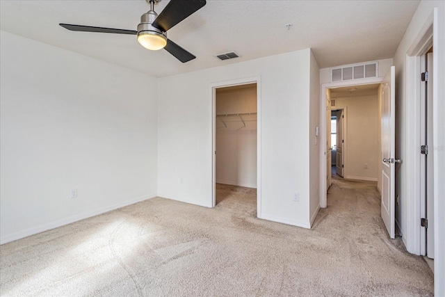 unfurnished bedroom featuring ceiling fan, light colored carpet, a spacious closet, and a closet