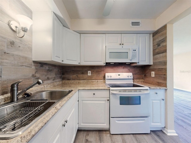 kitchen featuring white appliances, white cabinetry, wooden walls, and sink