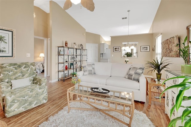 living room with light hardwood / wood-style flooring, high vaulted ceiling, and ceiling fan with notable chandelier