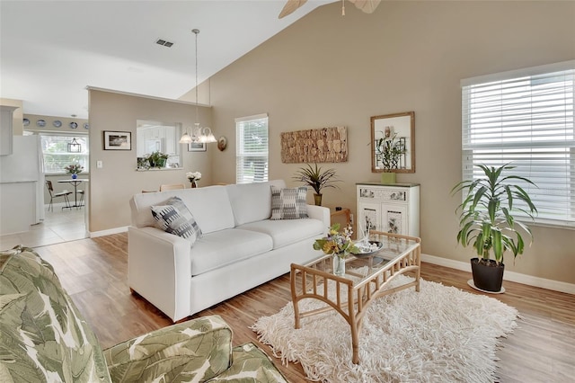 living room featuring ceiling fan with notable chandelier, wood-type flooring, and vaulted ceiling