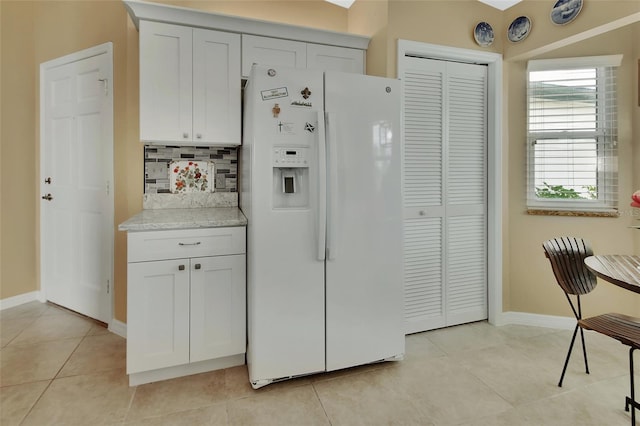 kitchen with white cabinets, white refrigerator with ice dispenser, light tile patterned floors, and tasteful backsplash