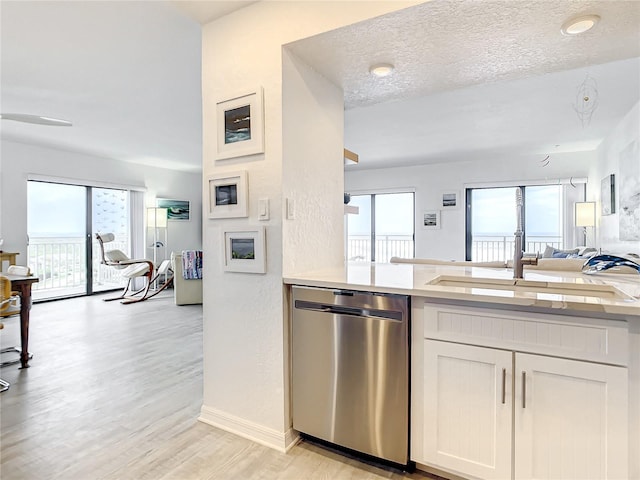 kitchen featuring white cabinets, light wood-type flooring, a textured ceiling, and stainless steel dishwasher