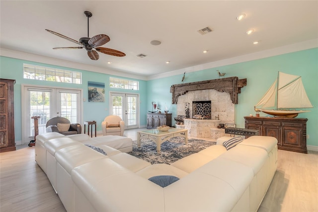 living room featuring ceiling fan, french doors, light wood-type flooring, a fireplace, and ornamental molding