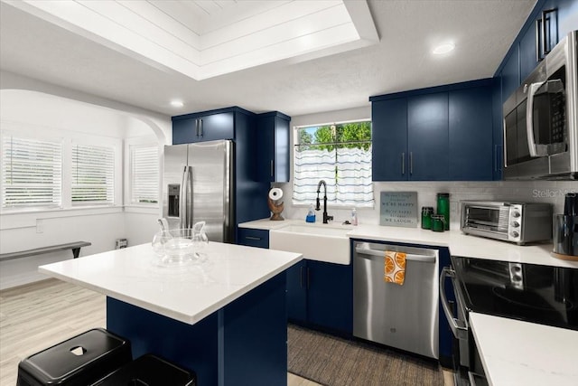 kitchen featuring sink, blue cabinetry, appliances with stainless steel finishes, a center island, and dark hardwood / wood-style flooring