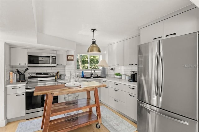 kitchen with sink, backsplash, stainless steel appliances, white cabinets, and decorative light fixtures