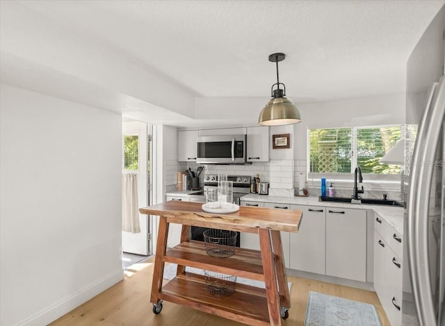 kitchen featuring sink, a wealth of natural light, pendant lighting, stainless steel appliances, and white cabinets