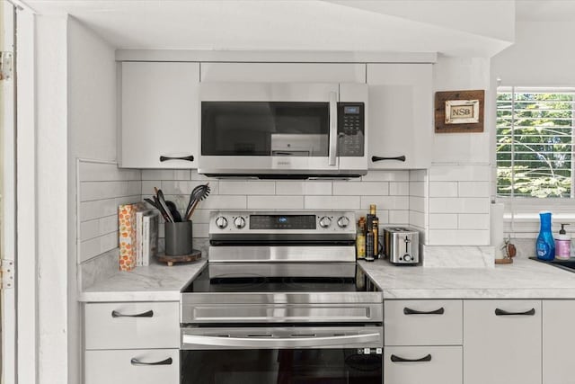 kitchen with tasteful backsplash, stainless steel appliances, light stone counters, and white cabinets