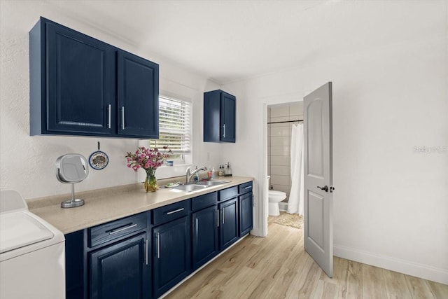 kitchen featuring blue cabinetry, light hardwood / wood-style floors, washer / dryer, and sink