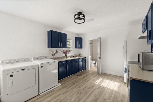 laundry area featuring sink, washing machine and clothes dryer, a textured ceiling, and light hardwood / wood-style flooring