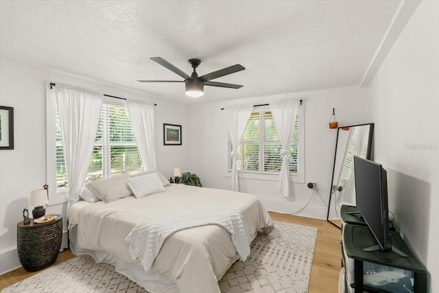 bedroom featuring multiple windows, a textured ceiling, ceiling fan, and light hardwood / wood-style flooring