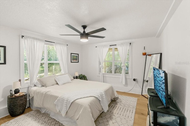 bedroom with ceiling fan, a textured ceiling, multiple windows, and light wood-type flooring